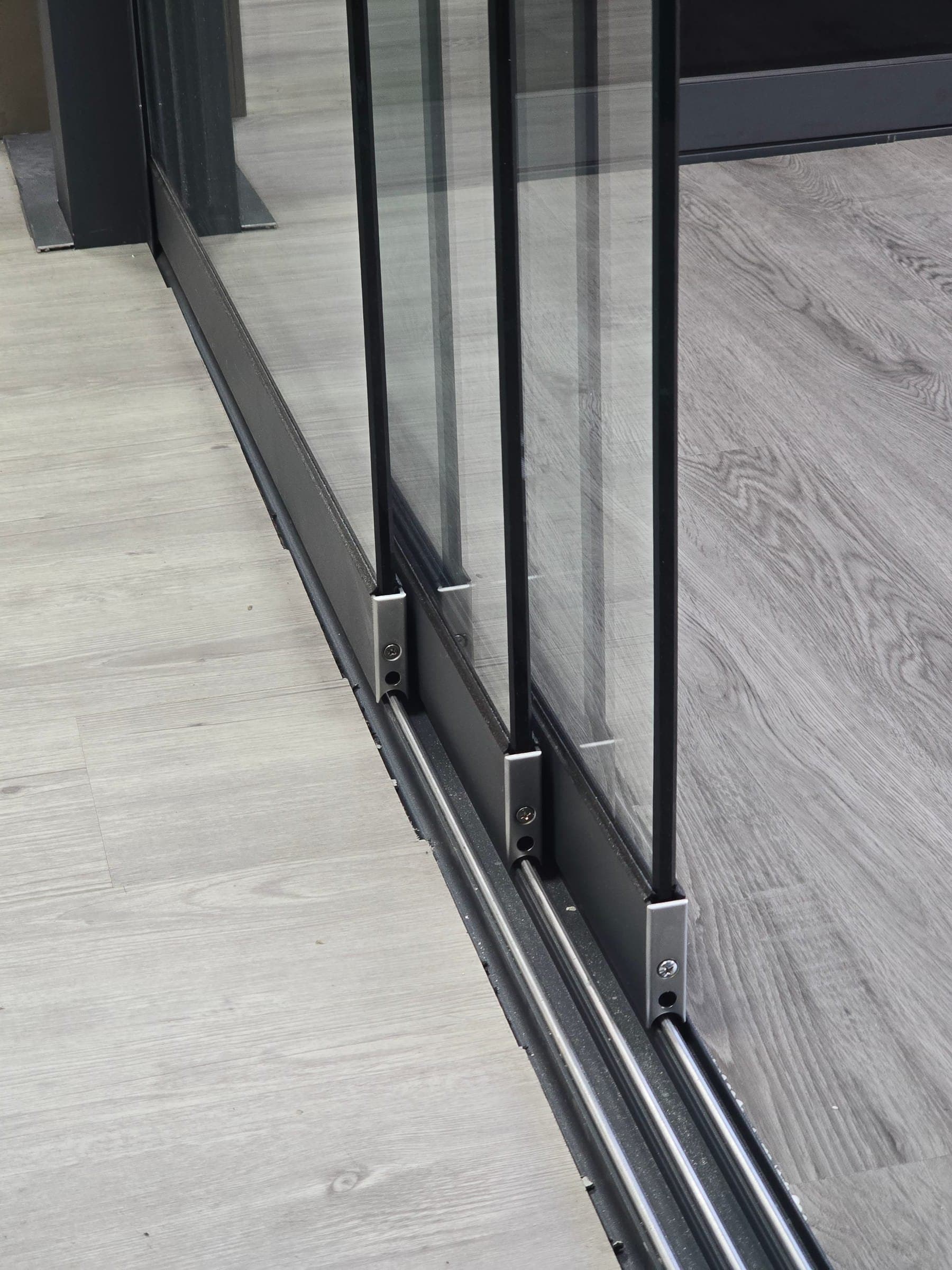 Close-up of frameless sliding glass doors running on a multi-track aluminium floor rail