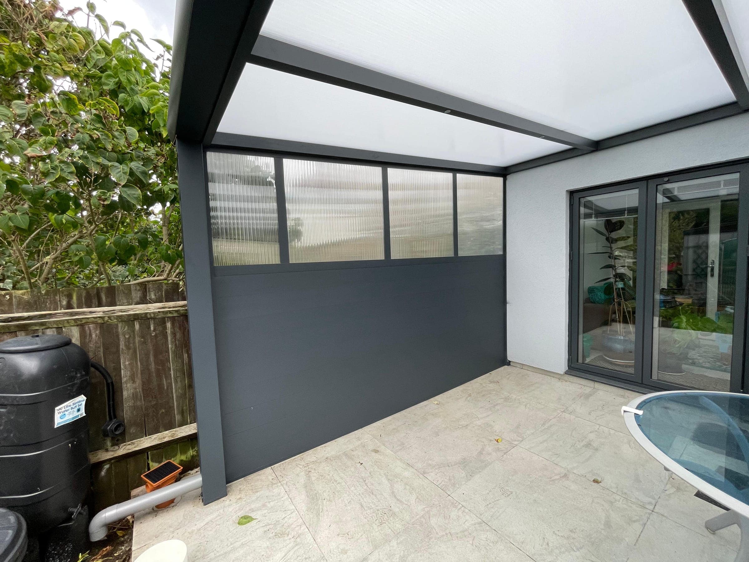 Integrated polycarbonate wedged wall enclosure on side of residential lean-to veranda showing translucent upper gable and solid framework