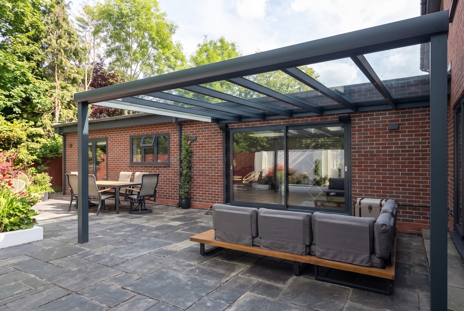 Anthracite grey aluminium veranda with clear laminated safety glass roof installed over a paved patio